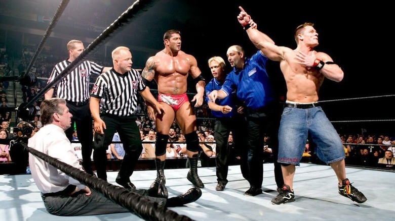 A referee raises John Cena's hand as Batista looks on in confusion and Vince McMahon sits on the ring canvas with an angry look on his face at the Royal Rumble in 2005.