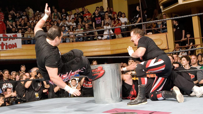 Terry Funk holds a trash can in front of Mick Foley, while Dreamer hits a dropkick