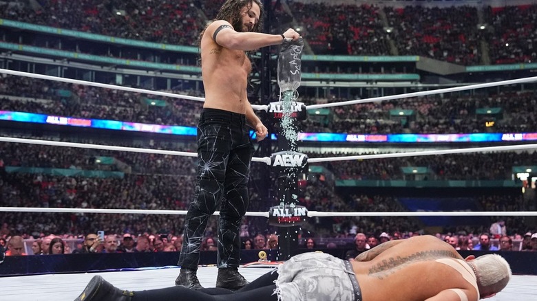 Jack Perry pours broken glass onto the mat beside Darby Allin