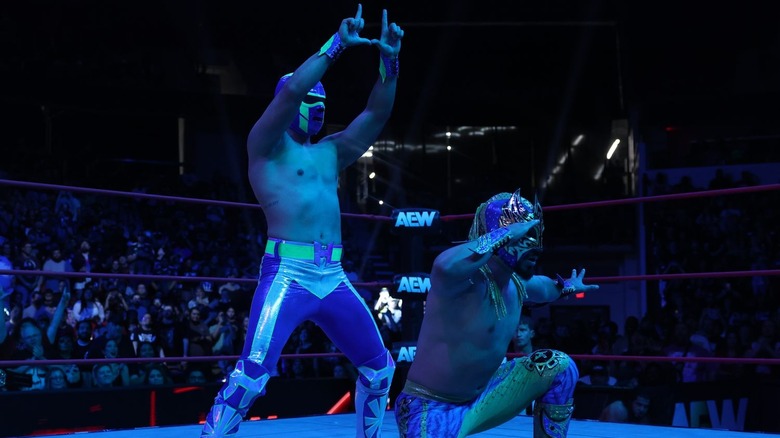 Hologram makes a H with his hands while Komander poses beside him on "AEW Collision"