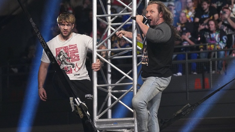 Will Ospreay and Kenny Omega standing on scaffolding, Omega with mic in hand, on "AEW Dynamite."