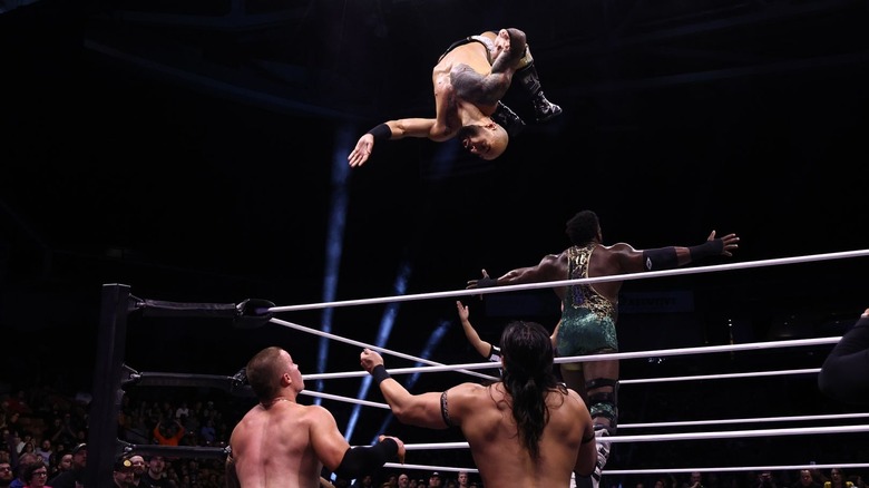 Powerhouse Hobbs poses while Ricochet flips over the top rope toward Kyle Fletcher and Konosuke Takeshita on the outside on "AEW Dynamite."