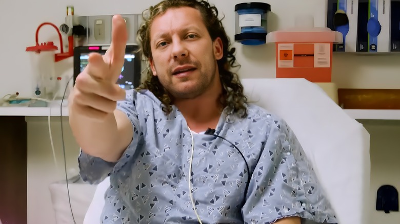 Kenny Omega in a hospital doing a finger gun