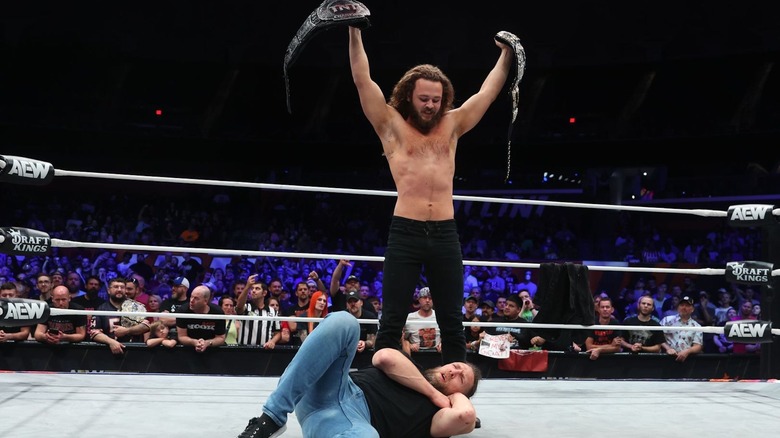 Jack Perry standing over Bryan Danielson with two title belts