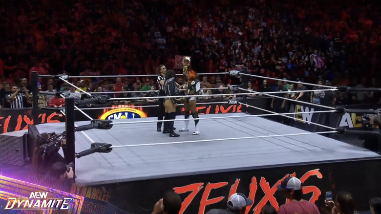 Mone holding up her TBS Championship and staring down Zeuxis