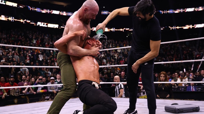 Jon Moxley holds Orange Cassidy as Wheeler Yuta pours liquid on his face at AEW Full Gear.