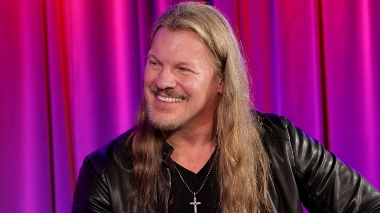 Chris Jericho smiling in front of a pink and purple curtain