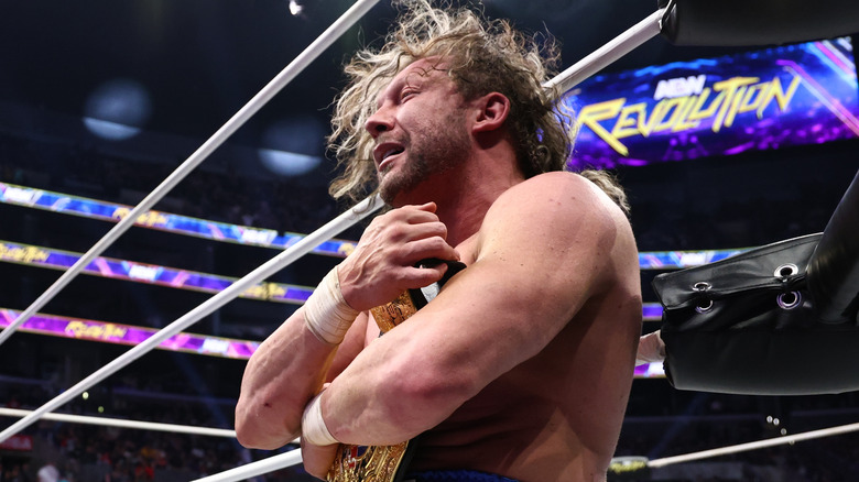 Kenny Omega hugs the International Championship to his chest while sitting on the ring apron after defeating Konosuke Takeshita at AEW Revolution.