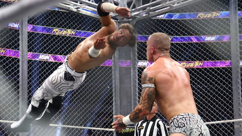 Will Ospreay looks to hit a cutter off the cage to Kyle Fletcher, who stands in the middle of the ring inside a steel cage during their match at AEW Revolution.