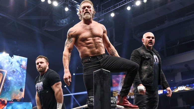 Adam Copeland stands in the ring on the top turnbuckle, flanked by FTR at AEW Worlds End