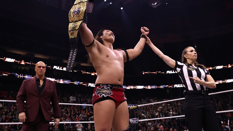 Konosuke Takeshita holds up the AEW International Championship alongside manager Don Callis and referee Aubrey Edwards at AEW Full Gear 2024.