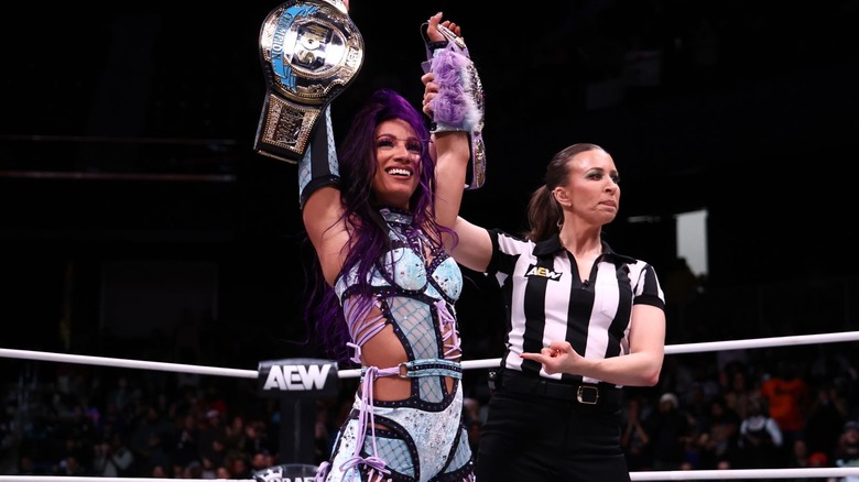 Mercedes Mone holding up her TBS title alongside referee Aubrey Edwards at "AEW Dynamite: Holiday Bash"