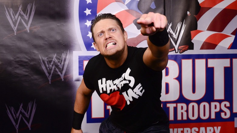 The Miz posing in front of a WWE Tribute to the Troops poster