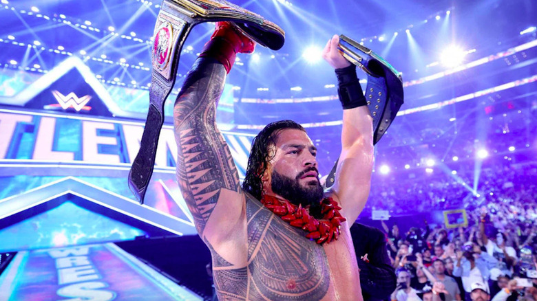 Roman Reigns holding up two championship titles