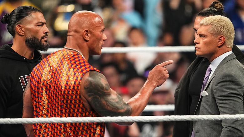 The Rock points a finger at Cody Rhodes as Roman Reigns and Seth Rollins look on.
