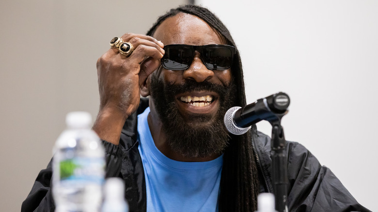 Booker T sitting behind a microphone smiling with sunglasses on