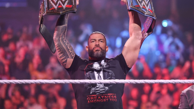 Roman Reigns raises his title belts