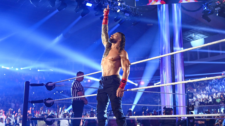 Roman Reigns standing outside wrestling ring, pointing to the sky