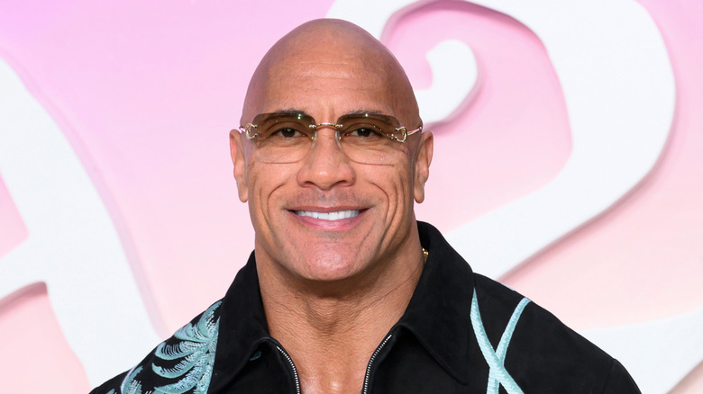 The Rock standing in front of a pink and white background