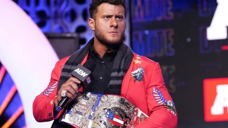 MJF holds a microphone and his American Championship while cutting a promo on the stage during an episode of AEW TV.