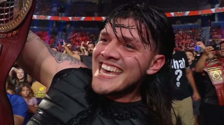 Dominik Mysterio smiles with the North American Championship on the outside of the WWE ring after defeating Sami Zayne.