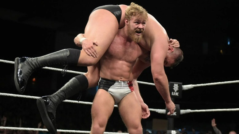 Tyler Bate holding WALTER in a fireman's carry