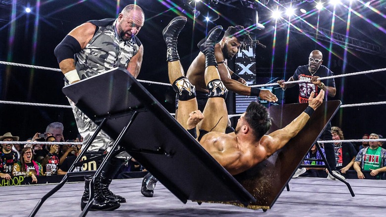 Bubba Ray Dudley and Trick Williams putting Ethan Page through a table during the NXT ECW Arena show while D-Von Dudley watches from the turnbuckle