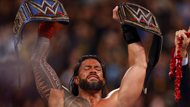 Roman Reigns holding his titles up high