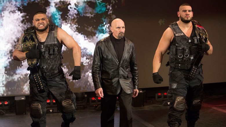 Akam and Rezar carry in the "NXT" Tag Team Championships alongside manager Paul Ellering.