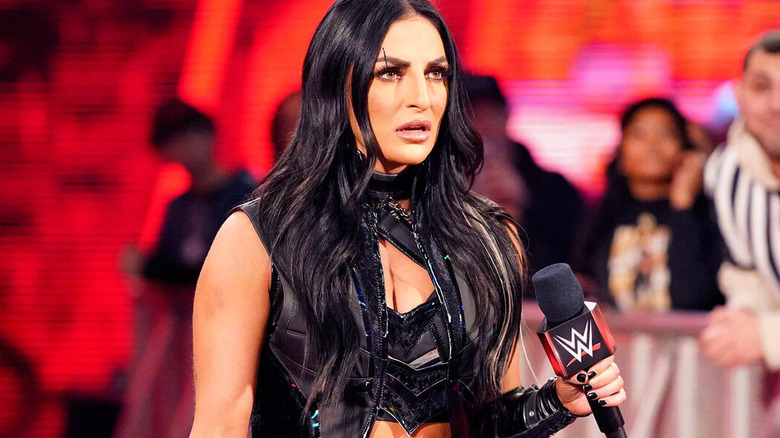 Sonya Deville glares ahead as she holds a WWE microphone in her hand.