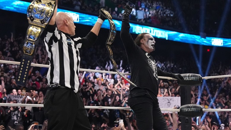 Referee holds up title belts while Sting celebrates