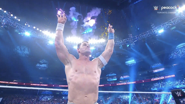 John Cena holds up his signature "OK" hand sign as fireworks erupt in the background.