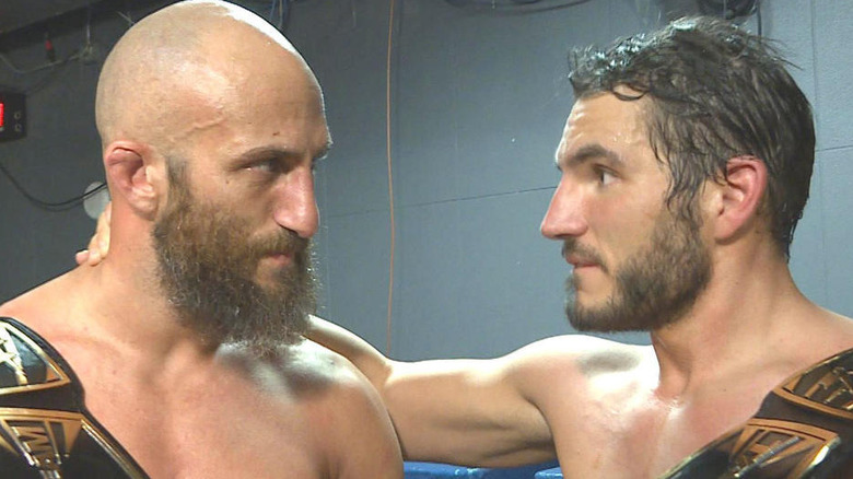 Tommaso Ciampa and Johnny Gargano face each other in a backstage hallway, holding the NXT Tag Team Championships.