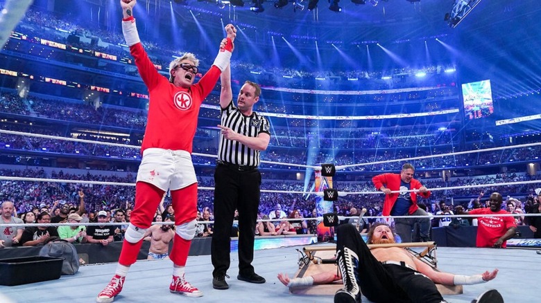 Johnny Knoxville has his hand raised by a referee while standing over Sami Zayn, following a victory at WrestleMania.