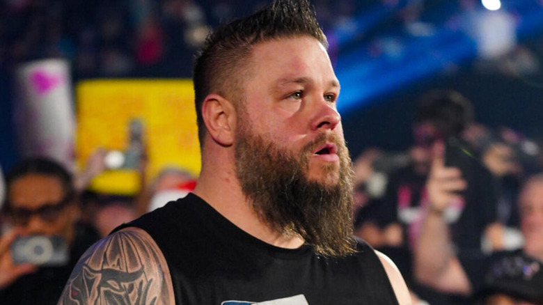 Kevin Owens wears a shirt with his face on it as he looks on.