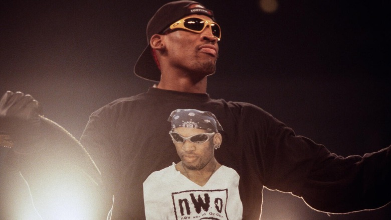 Dennis Rodman posing witht he WCW World Heavyweight Championship while wearing an nWo shirt.