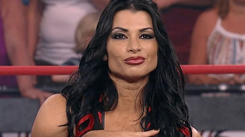 Tara stands in the ring, smirking, during a match on TNA programming.