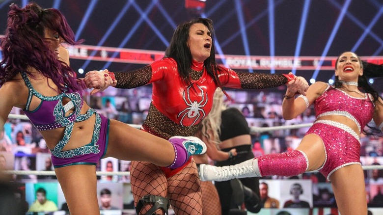 Victoria stands in the ring during the 2021 Royal Rumble match, being stretched out between Billie Kay and Peyton Royce.