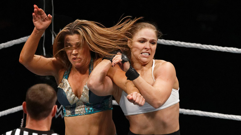 Mickie James grapples with Ronda Rousey as a referee looks on
