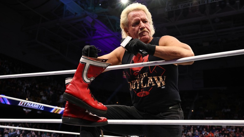 Jeff Jarrett holds his boots in one hand and a microphone in the other as he leans on the ropes.