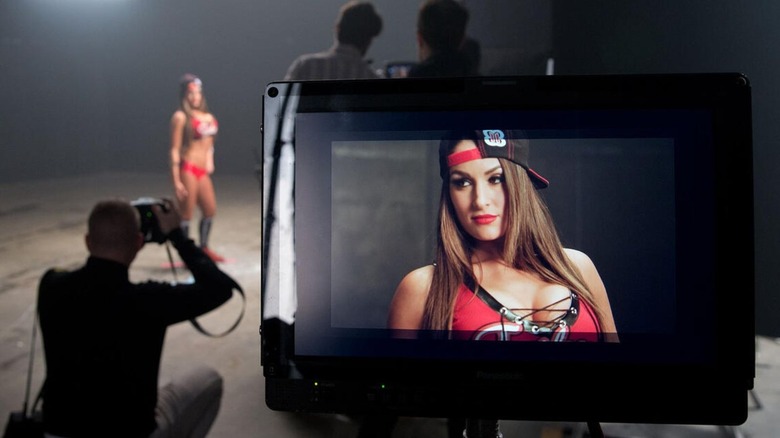 Nikki Bella poses backstage for a WWE.com photoshoot, and the camera lens sits in the foreground of the image.