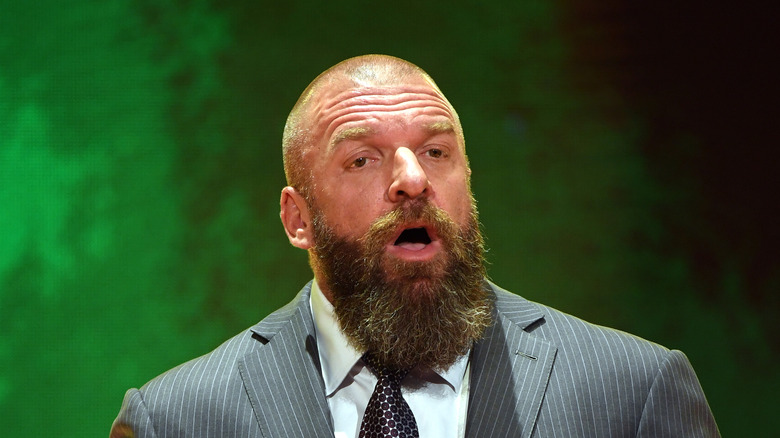 Triple H talking in front of a forest green background