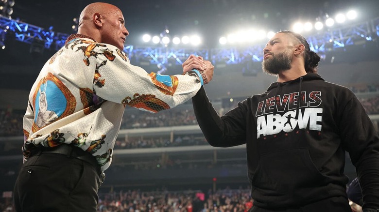 The Rock and Roman Reigns shake hands in the middle of the ring