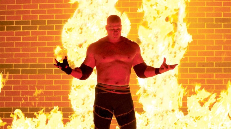 Kane stands in front of a flame for a photoshoot for WWE.com.