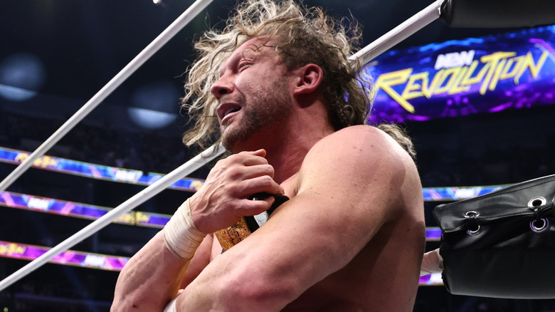 Kenny Omega clutches his newly one International Championship to his chest while sitting on the apron of the ring after his match at AEW Revolution.