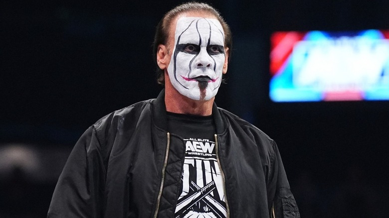 Sting standing in wrestling ring wearing AEW shirt and jacket