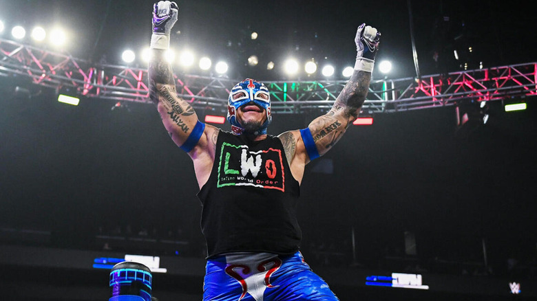 Rey Mysterio smiles as he holds up his arms.