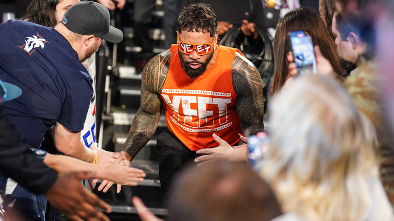 Jey Uso entering through the crowd in an orange Yeet shirt