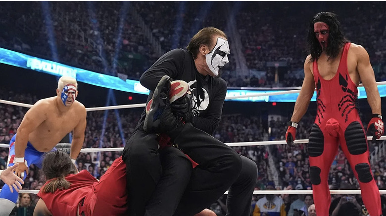 Sting locks The Young Bucks in a double Scorpion Death Drop as his sons look on.