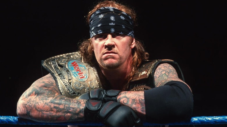 The Undertaker posing with the WWE World Tag Team Championships and the WWE Championship